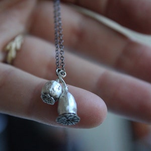 Op de afbeelding: Een zilveren ketting met een bedel van twee papaverzaaddozen.