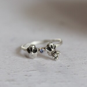 May include: A silver ring with two small, detailed figures and a blue gemstone in the center.