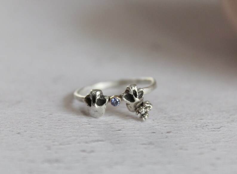 May include: A silver ring with two small, detailed figures and a blue gemstone in the center.
