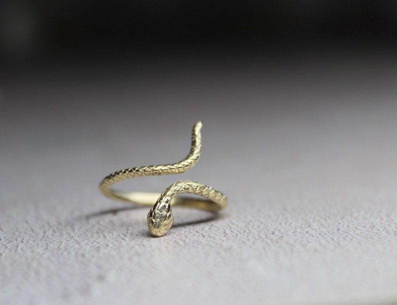 May include: A gold snake ring with a textured finish. The snake is coiled around the ring band and the head is facing forward.