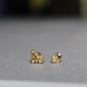 Peut inclure: Une paire de boucles d'oreilles en or, l'une avec une petite pierre rose et l'autre avec un motif floral.