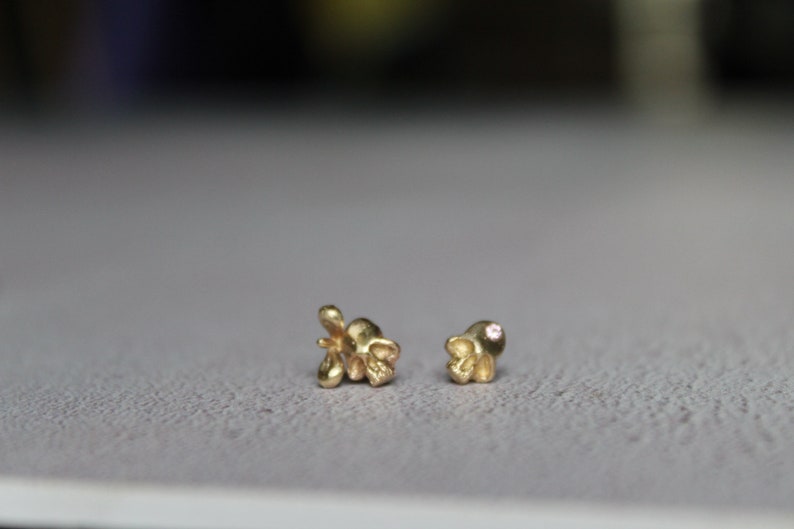 Peut inclure: Une paire de boucles d'oreilles en or, l'une avec une petite pierre rose et l'autre avec un motif floral.