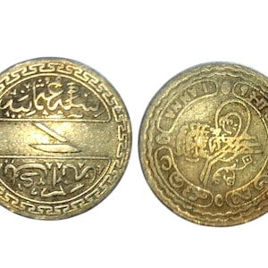 Puede incluir: Dos monedas antiguas de oro. La moneda de la izquierda presenta escritura árabe y un diseño estilizado. La moneda de la derecha tiene un emblema central rodeado de más escritura árabe y un borde decorativo. Ambas monedas tienen un aspecto desgastado.