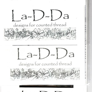 May include: A black and white image of a logo for a counted thread design company called "La-D-Da". The logo features a floral border and the text "designs for counted thread".