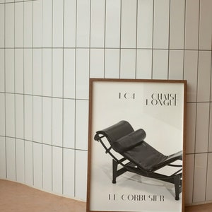 May include: A black and white poster with a brown wooden frame. The poster features a black leather chaise lounge with a black pillow. The text on the poster reads "LC4 CHAISE LONGUE LE CORBUSIER".