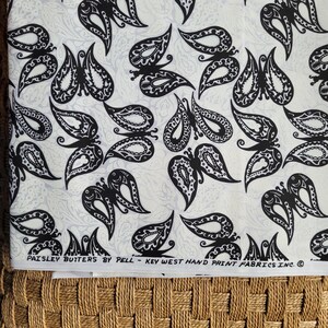 May include: White fabric with a black paisley butterfly pattern. The fabric has the text "Paisley Butters by Pell - Key West Hand Print Fabrics Inc. ©" printed on it.