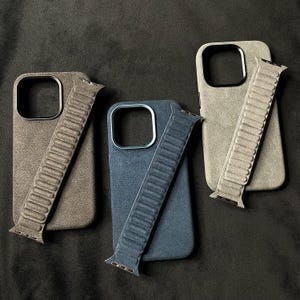 May include: Three phone cases with matching bands. The cases are made of a soft, textured material and come in grey, blue, and brown.