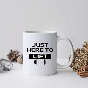 May include: White ceramic mug with a black graphic that says "Just Here To Lift" with a dumbbell icon.