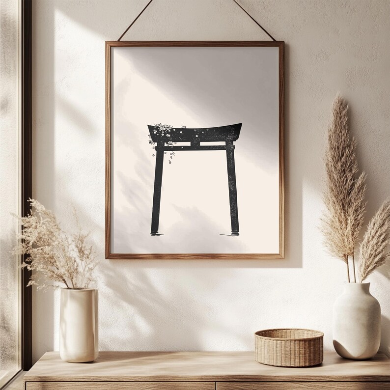 May include: Black and white minimalist print of a traditional Japanese torii gate with a vine of flowers growing on top. The print is framed in a simple black frame and hanging on a white wall.