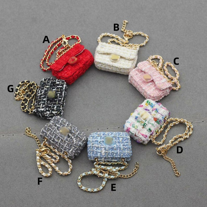 Puede incluir: Una colecci&oacute;n de peque&ntilde;os bolsos de mano en varios colores, incluyendo rojo, blanco, rosa y azul. Cada bolso presenta una tela texturizada y una correa de cadena dorada. Los bolsos est&aacute;n dispuestos en un patr&oacute;n circular.