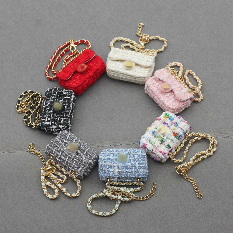 Puede incluir: Una colecci&oacute;n de peque&ntilde;os bolsos de mano en varios colores, incluyendo rojo, blanco, rosa, negro, gris, azul y multicolor. Cada bolso presenta una correa de cadena dorada y un cierre de broche, con tejido tipo tweed.