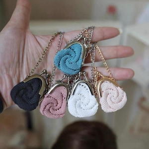 May include: A collection of small, crocheted coin purses in various colors, including black, blue, pink, and white. Each purse features a metal clasp and chain. The purses are held in a hand.