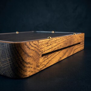 Puede incluir: Una base de exhibici&oacute;n rectangular de madera con un patr&oacute;n de veta natural prominente y esquinas redondeadas. La superficie superior est&aacute; cubierta por un panel acr&iacute;lico transparente asegurado con peque&ntilde;os tornillos met&aacute;licos color lat&oacute;n.