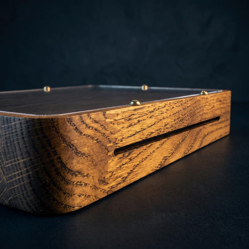 Puede incluir: Una base de exhibici&oacute;n rectangular de madera con un patr&oacute;n de veta natural prominente y esquinas redondeadas. La superficie superior est&aacute; cubierta por un panel acr&iacute;lico transparente asegurado con peque&ntilde;os tornillos met&aacute;licos color lat&oacute;n.