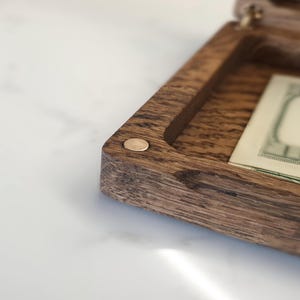 "Premium oak money box closed with 'Wedding Fund' engraving on top, ideal birthday gift."
"Open oak money box with brass hinges, holding U.S. dollar bills, perfect for holidays."
"Close-up of custom 'Love Always' engraving inside oak money box lid, a unique gift."
"Hand holding oak money box, showcasing its 7.9 x 4.3-inch size and natural wood grain."
"Oak money box with brass hinges on white surface, great for special occasion gifts."