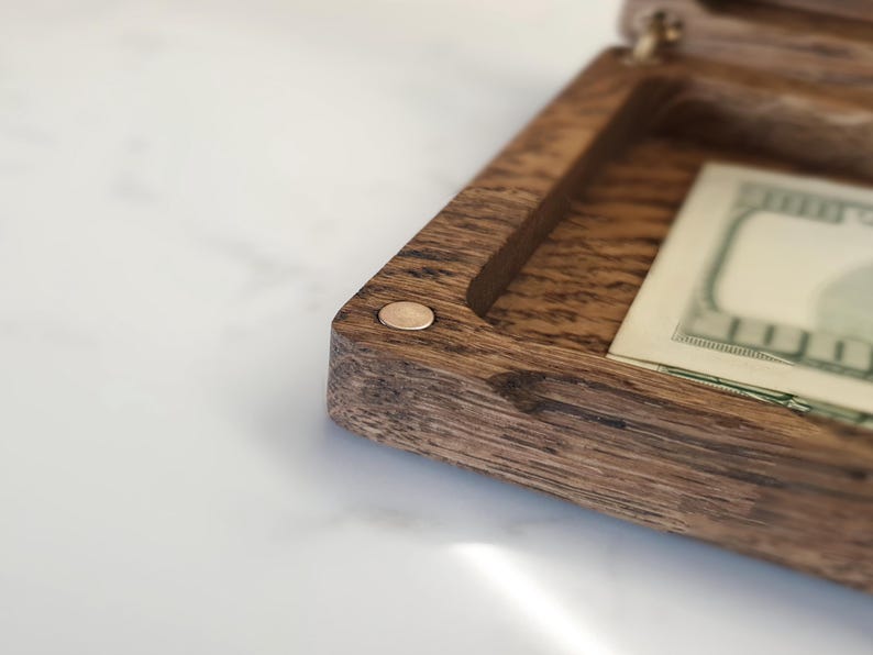 "Premium oak money box closed with 'Wedding Fund' engraving on top, ideal birthday gift."
"Open oak money box with brass hinges, holding U.S. dollar bills, perfect for holidays."
"Close-up of custom 'Love Always' engraving inside oak money box lid, a unique gift."
"Hand holding oak money box, showcasing its 7.9 x 4.3-inch size and natural wood grain."
"Oak money box with brass hinges on white surface, great for special occasion gifts."