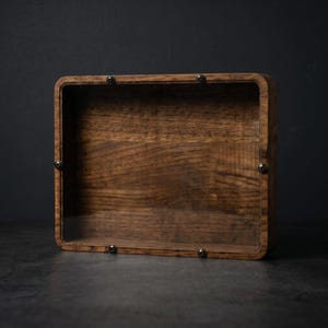 Puede incluir: Una caja de exhibici&oacute;n rectangular de madera con un acabado de veta de madera marr&oacute;n oscuro y un panel frontal transparente. El panel est&aacute; asegurado al marco de madera mediante cuatro peque&ntilde;os tornillos de metal oscuro en las esquinas.