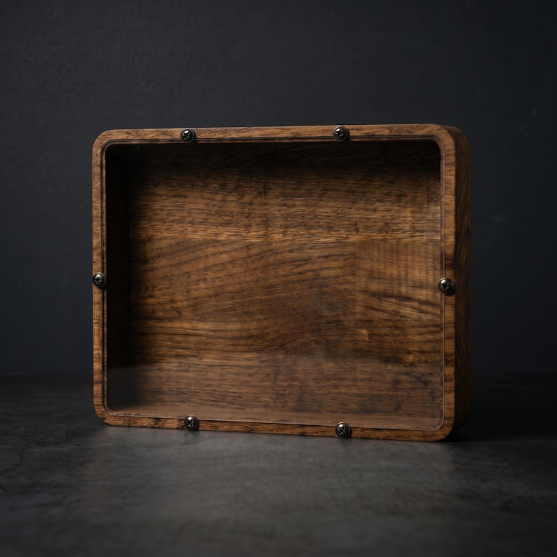 Puede incluir: Una caja de exhibici&oacute;n rectangular de madera con un acabado de veta de madera marr&oacute;n oscuro y un panel frontal transparente. El panel est&aacute; asegurado al marco de madera mediante cuatro peque&ntilde;os tornillos de metal oscuro en las esquinas.