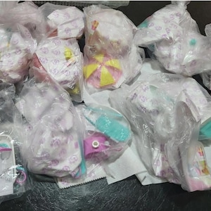 Könnte beinhalten: Eine Auswahl an Babyartikeln, darunter Windeln, Spielzeug und Zubehör, ist in transparenten Plastiktüten verpackt. Die Artikel sind in verschiedenen Farben erhältlich, darunter Rosa, Gelb und Blau. Einige Artikel sind sichtbar, wie z. B. ein Spielzeugschirm.