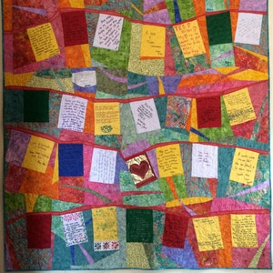 May include: A colorful quilt with a patchwork design. The quilt is made up of different fabrics in shades of red, orange, yellow, green, blue, and purple. Each square of the quilt has a handwritten message on it. The quilt is a beautiful and unique piece of art.