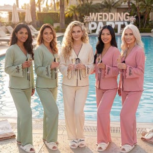 May include: Five people wearing coordinated pyjama sets in green, cream, and pink stand by a swimming pool. Each set includes a top and trousers. The tops have embroidered names on the cuffs. A "Wedding Party" sign is visible in the background.