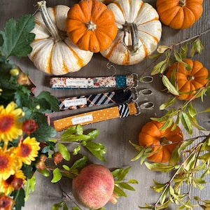 May include: Three colorful fabric keychains with the text "CLAMP & CLICK CO" on each. The keychains are displayed on a wooden surface with pumpkins and a pomegranate.