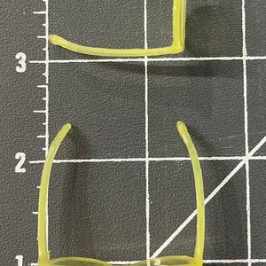 May include: Two pairs of neon yellow eyeglasses frames are displayed on a black grid surface. The frames are positioned with the top pair oriented horizontally and the bottom pair vertically. Each frame measures approximately 5 inches in length.