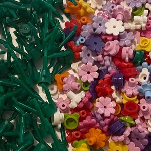 May include: A large collection of green plastic flower stems and colourful plastic flower heads. The flower heads are in various colours, including pink, purple, red, orange, yellow, and blue.