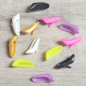 Peut inclure: Une collection de chaussures à talons hauts miniatures et d'accessoires en forme de chaussures de différentes couleurs, dont le blanc, l'or, le rose, le violet, le jaune et le noir. Les chaussures ont un design de pompe classique.