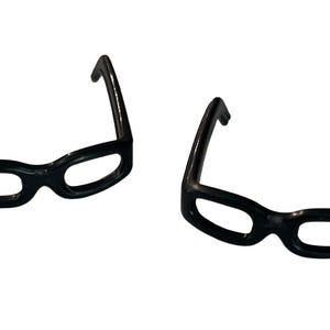 May include: Two pairs of black, thick-framed eyeglasses are displayed against a white background. The glasses have a classic, rounded shape with a glossy finish. The frames are a solid, opaque black.