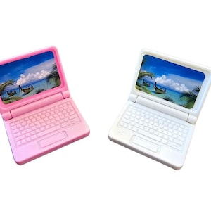 Könnte beinhalten: Zwei Spielzeug-Laptop-Computer, einer rosa und einer weiß, mit einer tropischen Strandkulisse auf dem Bildschirm.