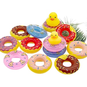 May include: A selection of inflatable donut-shaped pool floats in various colours, including pink, yellow, red, and blue, with sprinkles and frosting details. Some floats feature a yellow rubber duck in the centre. Ideal for summer fun and pool parties.