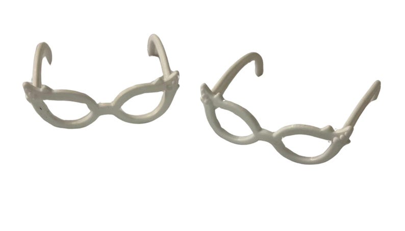 May include: Two pairs of white, decorative eyeglasses with a whimsical design. The frames have a rounded shape with decorative accents near the temples. The glasses are set against a plain white background.