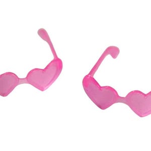 May include: Two pairs of pink heart-shaped sunglasses. The frames and lenses are a translucent pink. The sunglasses are a fun accessory, perfect for a themed party or a playful look.
