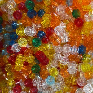 Könnte beinhalten: Eine große Ansammlung kleiner, kreisförmiger, durchscheinender Kunststoff-Bausteine in verschiedenen leuchtenden Farben wie Rot, Orange, Gelb, Grün, Blau und Transparent. Jedes Teil hat einen Noppen auf der Oberseite.