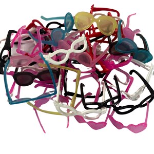 May include: A pile of small, colorful toy sunglasses in various shades, including black, white, pink, blue, and yellow. The sunglasses have different frame styles and are made of plastic. The image is taken against a white background.