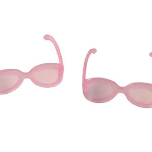 May include: Two pairs of light pink sunglasses with rounded frames and curved temples. The lenses are a lighter shade of pink. The sunglasses are set against a white background.
