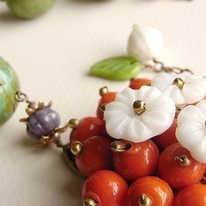 May include: A necklace with a variety of beads, including turquoise, green, white, and orange. The necklace features white flower-shaped beads with gold accents.