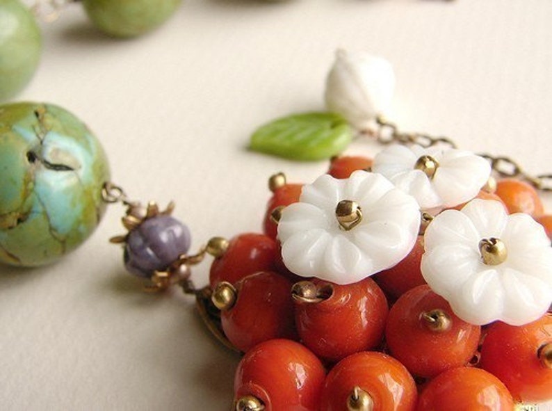 May include: A necklace with a variety of beads, including turquoise, green, white, and orange. The necklace features white flower-shaped beads with gold accents.