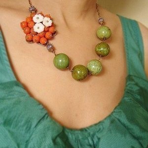 May include: A copper necklace with a cluster of orange and white flowers and a strand of green and brown beads.
