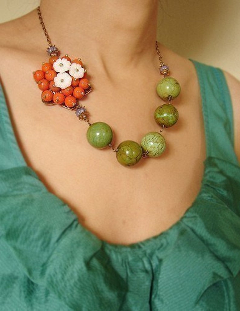 May include: A copper necklace with a cluster of orange and white flowers and a strand of green and brown beads.