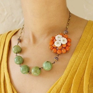May include: A necklace with a large orange and white flower pendant and a strand of green beads.