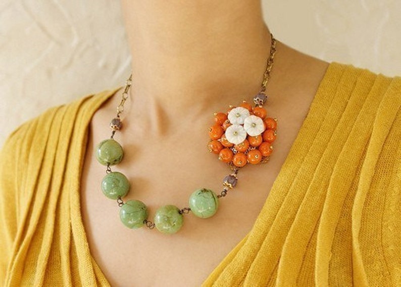May include: A necklace with a large orange and white flower pendant and a strand of green beads.