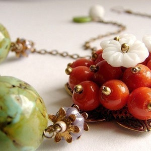 May include: A necklace with a pendant made of orange and white beads. The pendant is shaped like a flower with a gold center. The necklace also has green and brown beads.