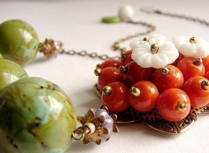 May include: A necklace with a pendant made of orange and white beads. The pendant is shaped like a flower with a gold center. The necklace also has green and brown beads.