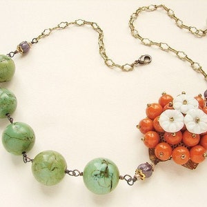 May include: A green and orange beaded necklace with a floral pendant. The pendant is made of white and orange beads and has a gold-tone setting.