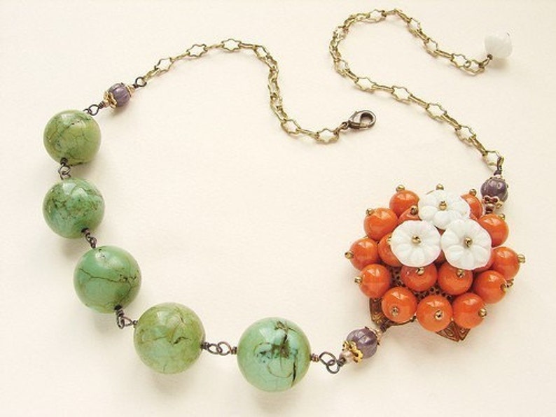May include: A green and orange beaded necklace with a floral pendant. The pendant is made of white and orange beads and has a gold-tone setting.