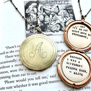 Może przedstawiać: Naszyjniki z medalionami w stylu vintage. Jeden medalion jest zamknięty grawerowaną literą "A". Drugi medalion jest otwarty, ukazując cytat "...ALE NIE MA SENSU WRACAĆ," a drugi z cytatem "PONIEWAŻ BYŁEM WTEDY INNĄ OSOBĄ, - ALICJA."