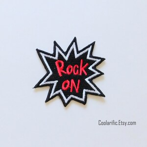 Puede incluir: Parche bordado en blanco y negro con un contorno blanco y un texto "Rock On" en rojo.