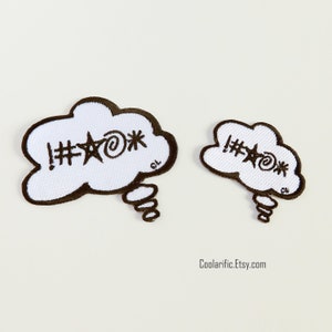 May include: Two white iron-on patches in the shape of a thought bubble with the text "!#@*" inside. The larger patch is approximately 3 inches wide and the smaller patch is approximately 2 inches wide.